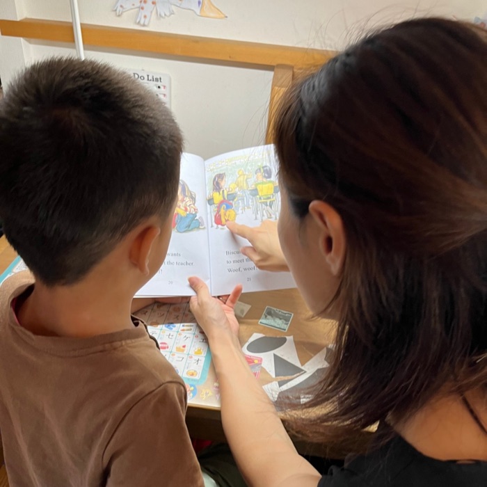 英語絵本のページを指さしながら、男の子に読み聞かせるお母さん